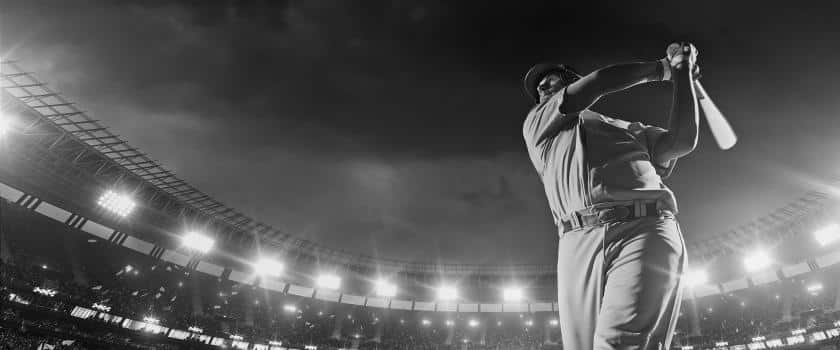 A black and white low shot picture of a man swinging a baseball bat in a full stadium of people 